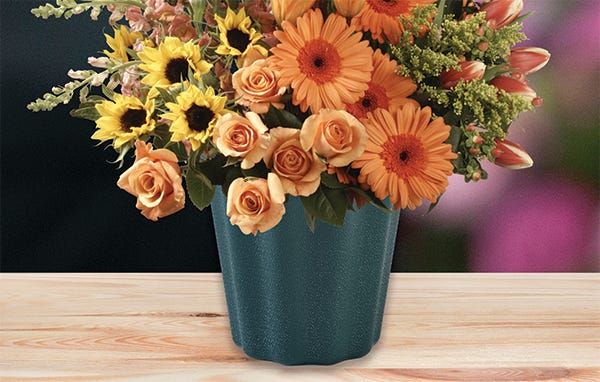 Orange and yellow flowers with greenery in a green cemetery vase on a butcher block tabletop