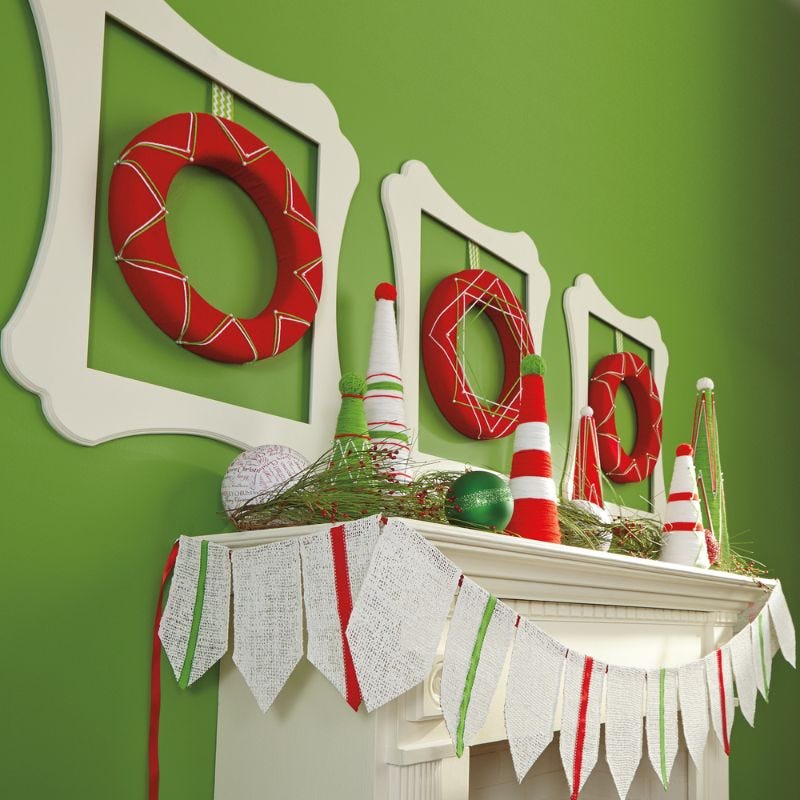 Red wreaths hanging in white square frames on a green wall over a fire place