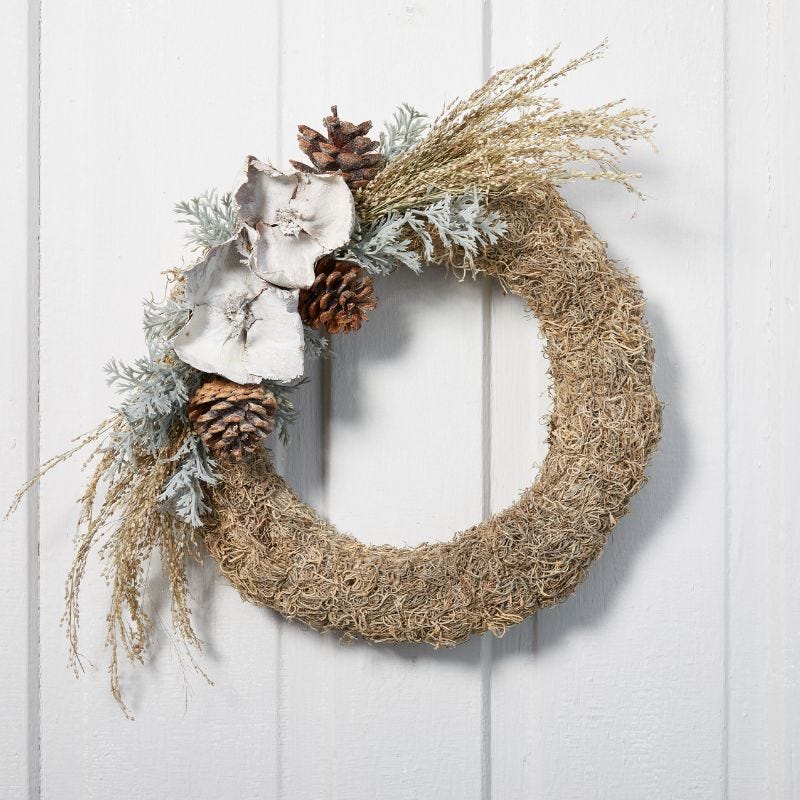 A round wreath decorated with natural florals, including spanish moss, greenery, and pinecones