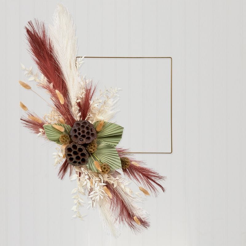 A gold square wreath decorated with dried florals