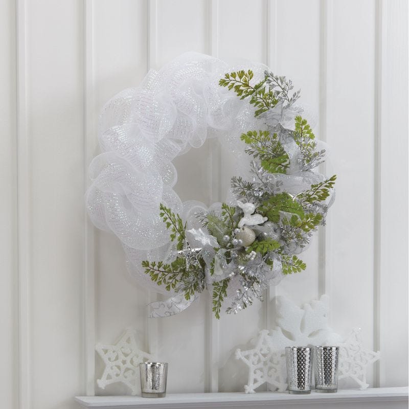 White and silver deco mesh wreath with greenery, ribbon, and other accents hung above a mantle