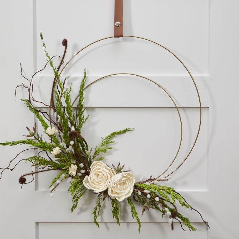 White flowers and greenery displayed on a round, wire wreath and hung on a door