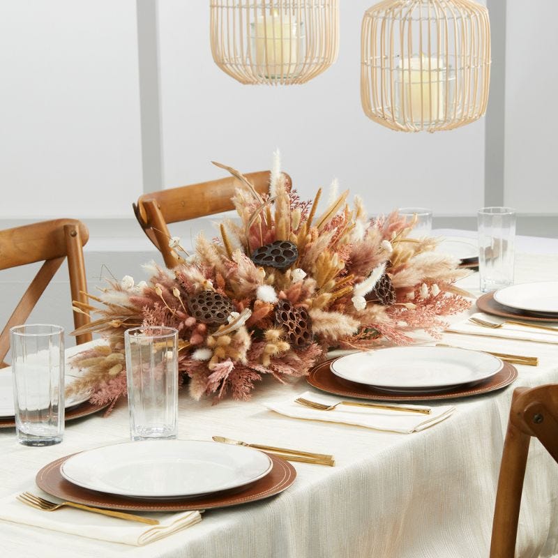 Dried floral arrangement in  neutral colors displayed in the center of dining table with chargers, platers, sliverware, and water glasses to create a tablescape