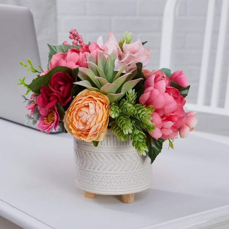 Pink and orange flowers mixes with greenery and a succulent in a potted floral display on a desktop
