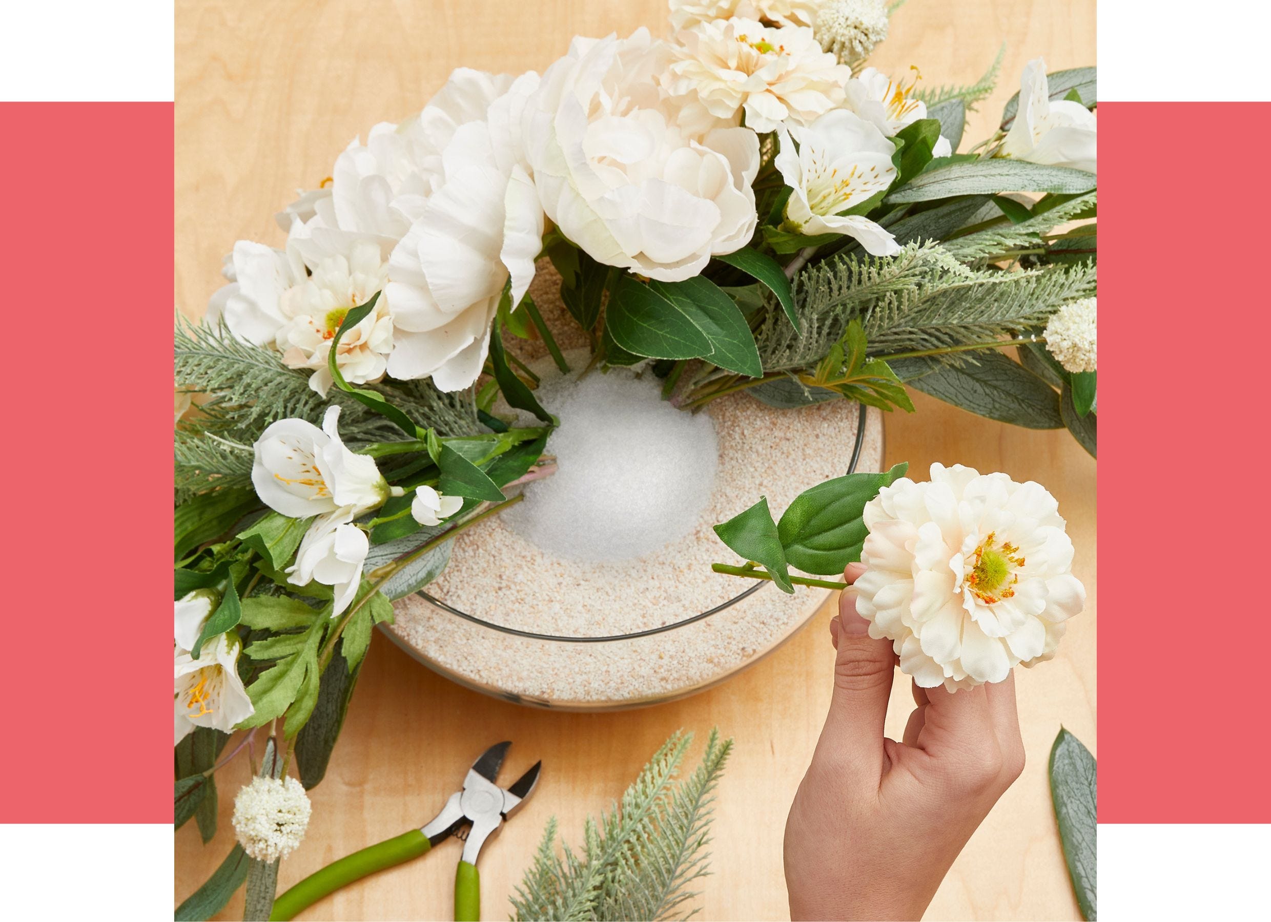 White flowers and greend are being arranged in a foam half ball in the center of a glass bowl vase on a table