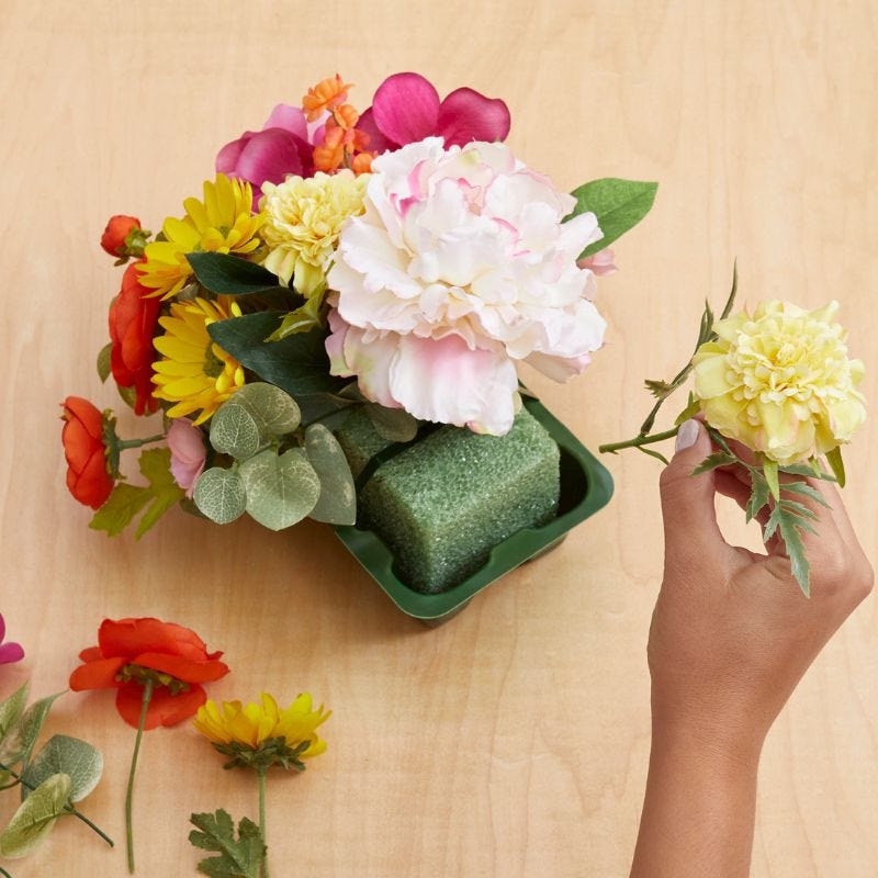 Color floral stems being inserted into a green floral foam block on a table
