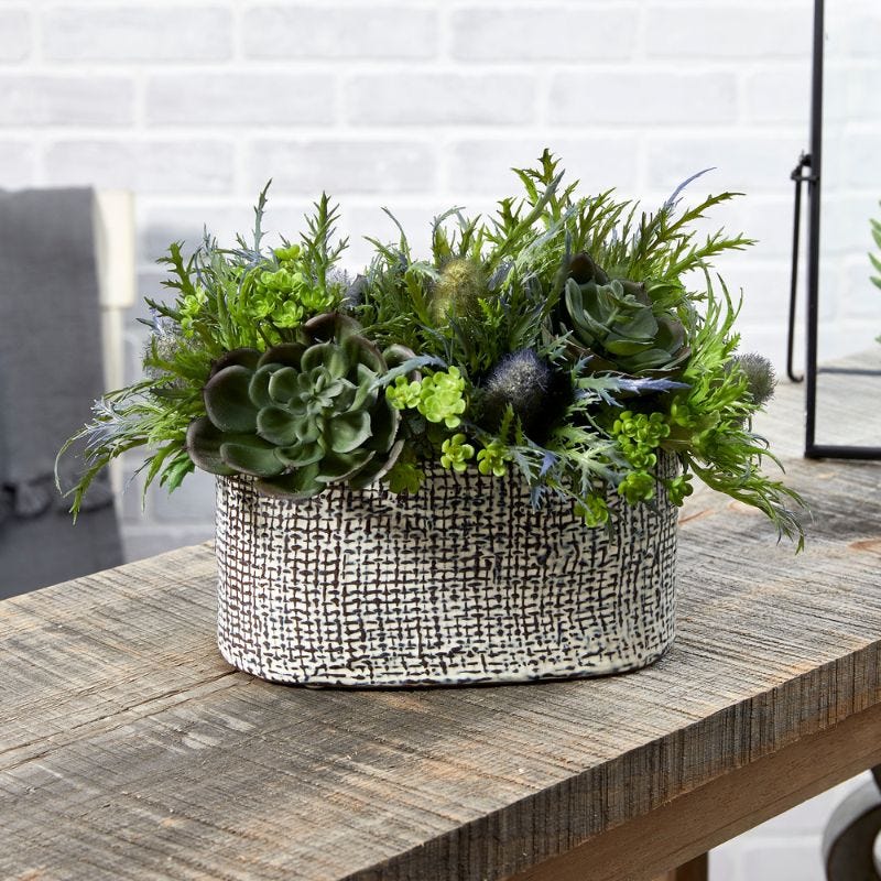 Greenery and succulents are arranted in a neutral colored containers that is displayed on an table