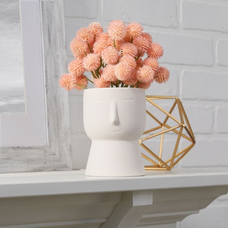 Peach colored flowers are arranged in a whimsical vase with a face