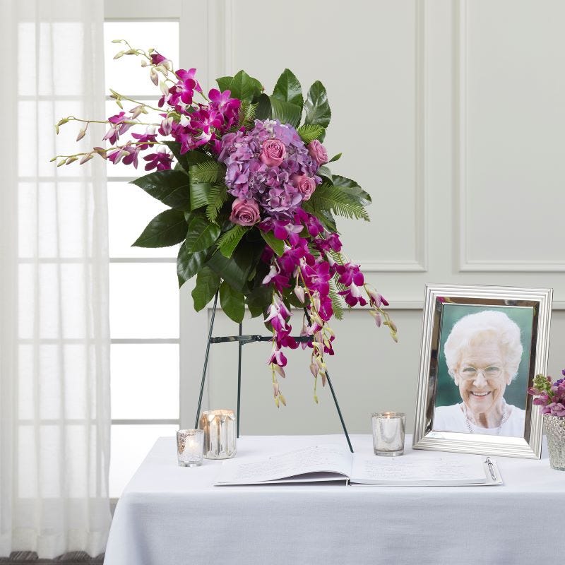 Pink and green memorial flower arrangement on a table with a photo, candles, and guest book