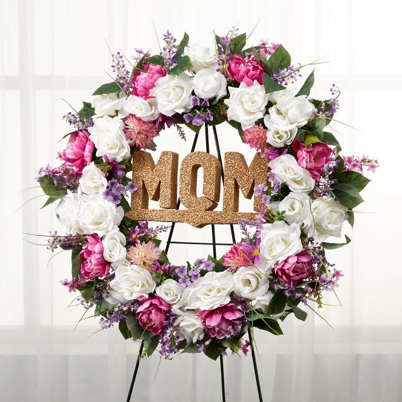 Pink, white, purple, and green floral memorial wreath displayed on an easel and featuring floral foam letters that spell MOM