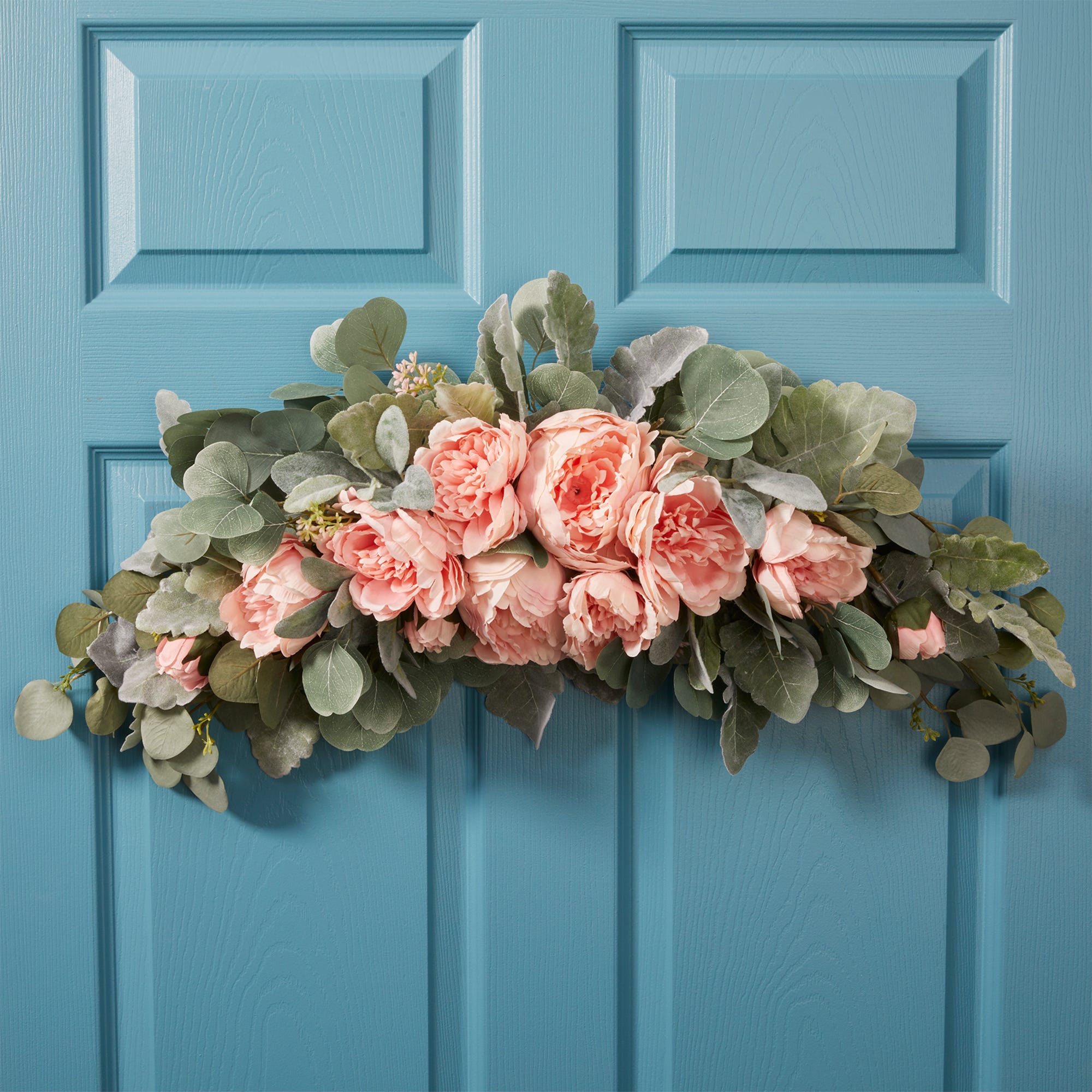 Blush colored roses and peonies with greenery on of floral foam swag wreath against a turquoise door