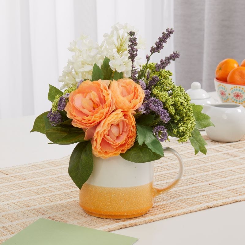 A floral arrangement with colors that pop for Mother's Day displayed in a coffee cup on a kitchen table