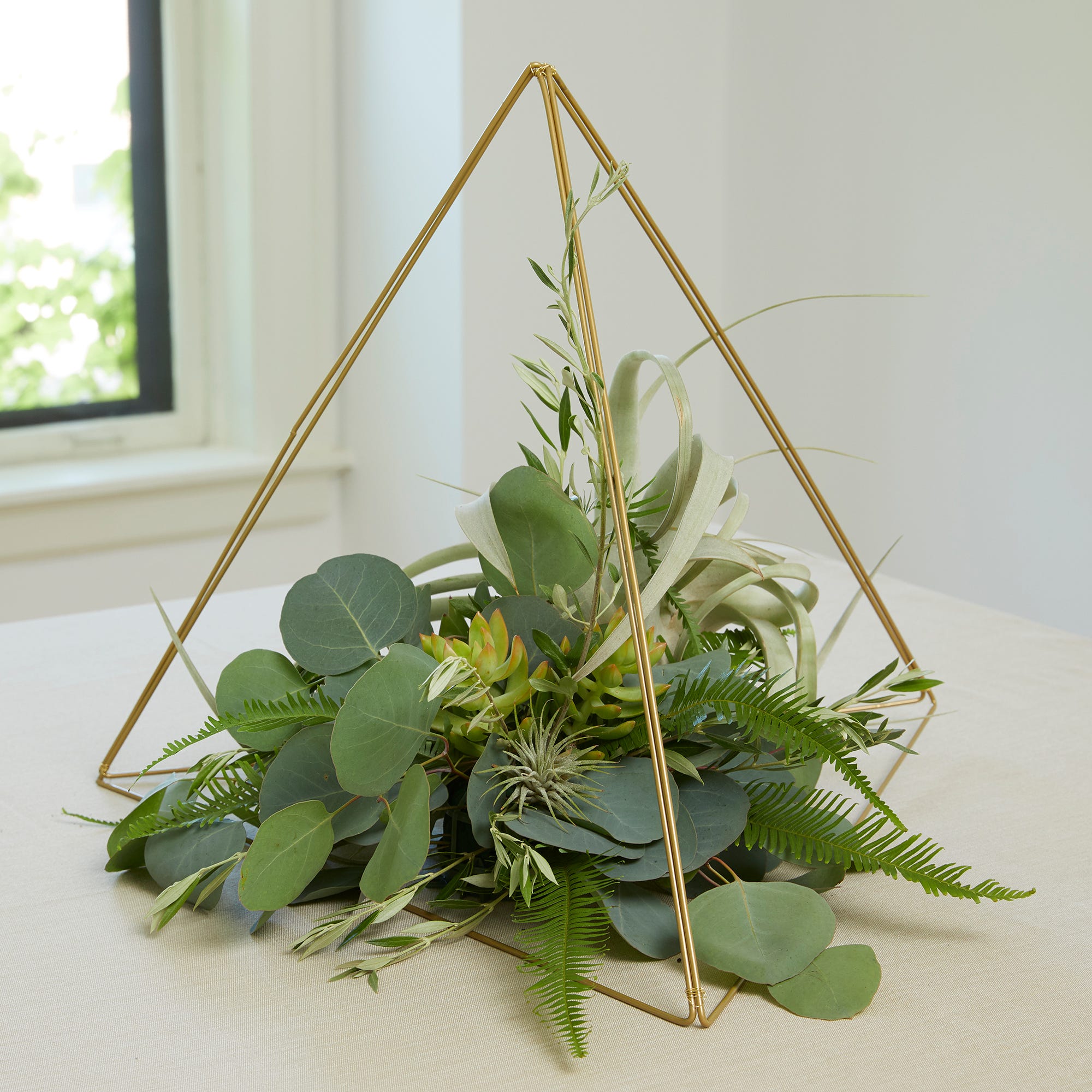 Greenery and succulents displayed within three gold frame wreaths to create a tabletop floral display