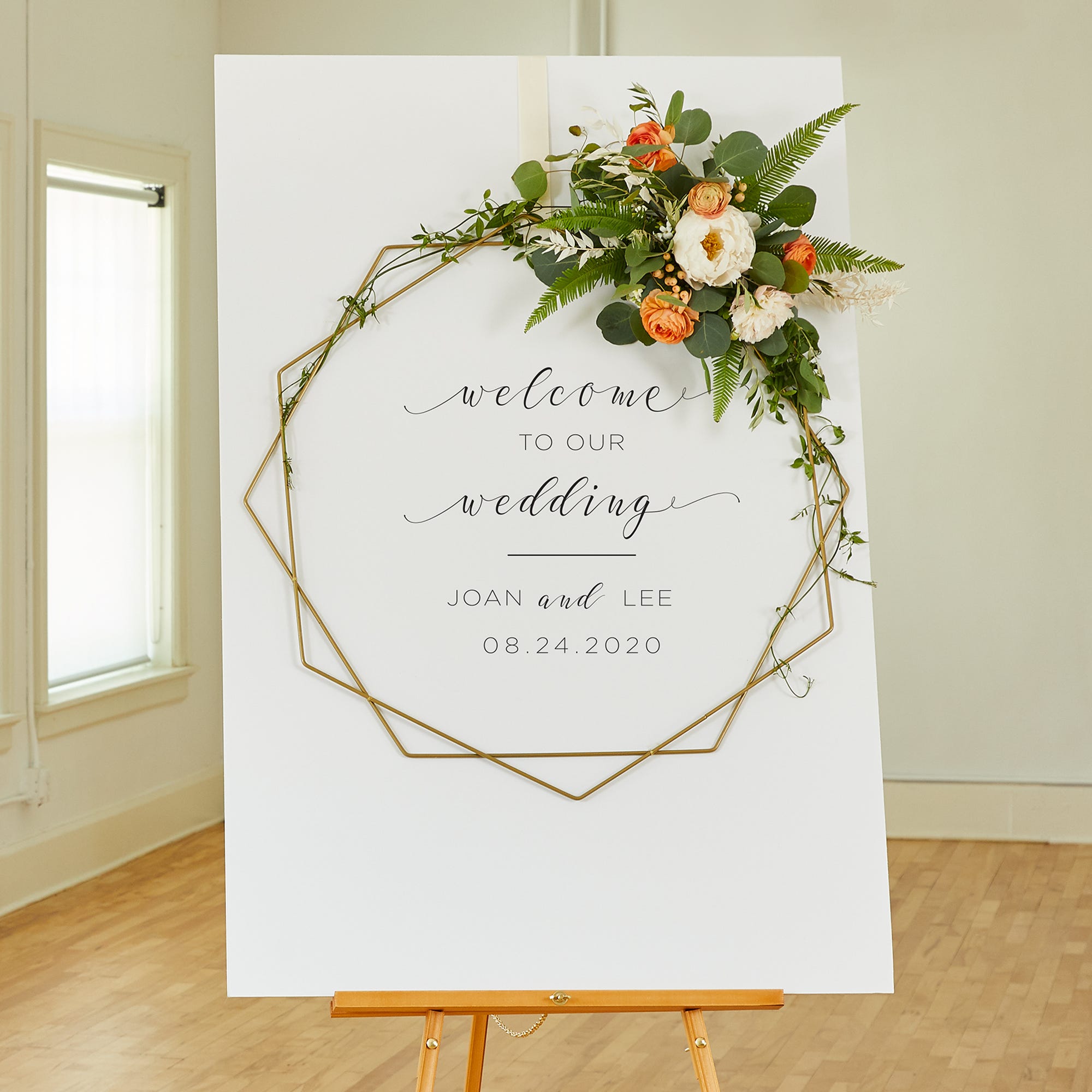 Gold wreaths with coral, cream, and green florals displayed on a Welcome to Our Wedding sign